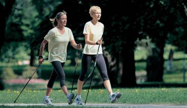 Zwei Frauen beim Nordic Walking auf einer grünen Wiese