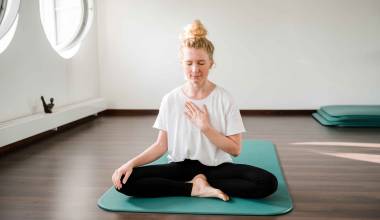 Frau sitzt auf Yoga Matte und meditiert