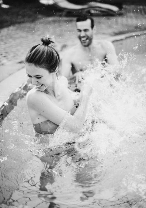 Lächelndes Paar spritzt sich mit Wasser im Außenpool