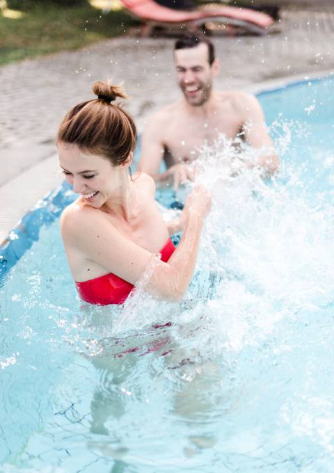 Lächelnde Frau spritzt mit Wasser in einem Außenpool