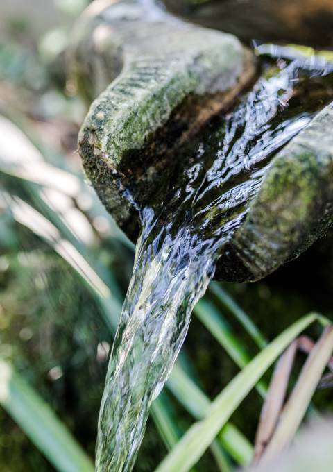 Sanftes Wasser fließt über Steine in einem Gartenbrunnen Beschreibung: Ein beruhigendes Wasserspiel im Garten