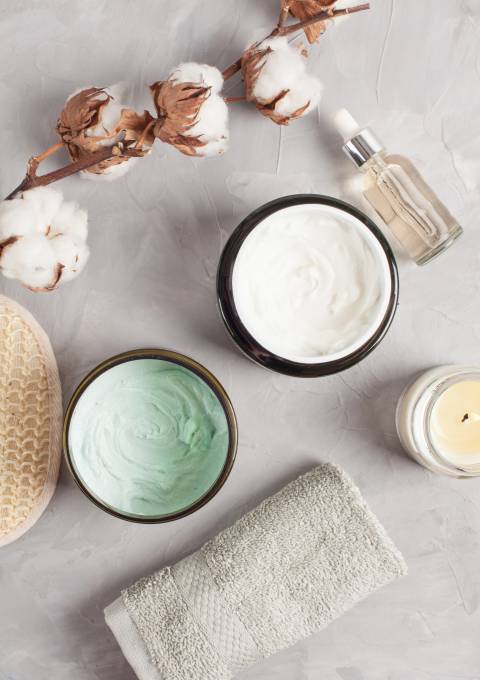 Schalen mit pflegenden Cremes und Kerzen auf einem Spa-Tisch