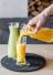 Person gießt frisch gepressten Orangensaft neben einem grünen Smoothie ein