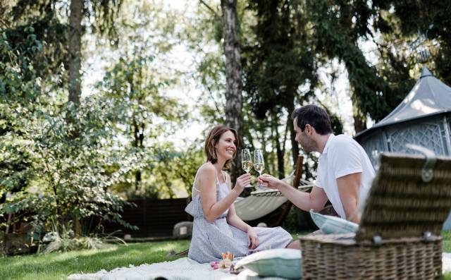 Paar genießt ein romantisches Picknick und stößt mit Sekt an im Garten des Antoniushofs