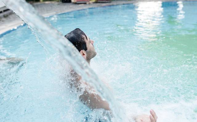 Mann entspannt unter einem erfrischenden Wasserstrahl im Außenpool.