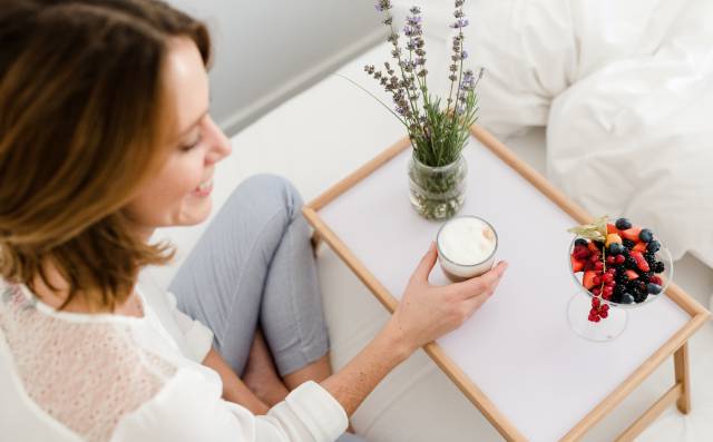 Frau genießt entspannt eine Tasse Kaffee mit frischen Beeren in einem gemütlichen Hotelzimmer